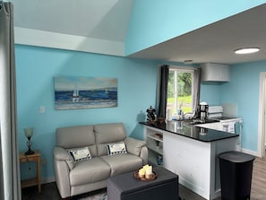 A modern kitchen with a central island, a dining area with a sofa and cushions, and a painting of a sailboat on the wall.