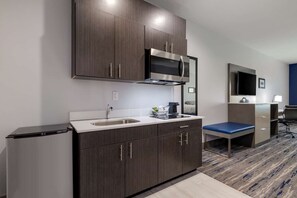 A compact kitchen with a microwave, sink, and cabinets, a small seating area, and a TV on a stand. - Best Western Plus Choctaw Inn & Suites (Choctaw)