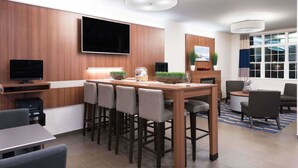 A modern hotel room with a wooden dining table, bar stools, a flat-screen TV, and a large window with curtains. - Microtel Inn & Suites By Wyndham Windham (Windham)