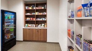 A vending machine with various beverages, a stocked shelf with snacks and drinks, and a storage cabinet. - Microtel Inn & Suites By Wyndham Windham (Windham)
