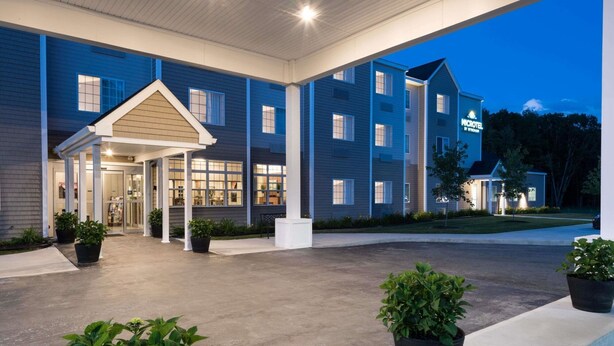 A hotel with a covered entrance, multiple windows, and potted plants. - Microtel Inn & Suites By Wyndham Windham (Windham)