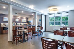 A restaurant with a bar area, multiple tables and chairs, and large windows offering a view of the outdoors. - Microtel Inn & Suites By Wyndham Windham (Windham)