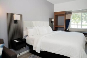 A hotel room with a large bed, a bedside table, a wall-mounted lamp, and a window with curtains. - Microtel Inn & Suites By Wyndham Windham (Windham)