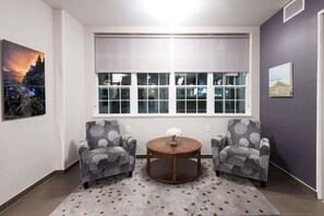A room with two armchairs, a round wooden table, a large window, and two wall-mounted paintings. - Microtel Inn & Suites By Wyndham Windham (Windham)