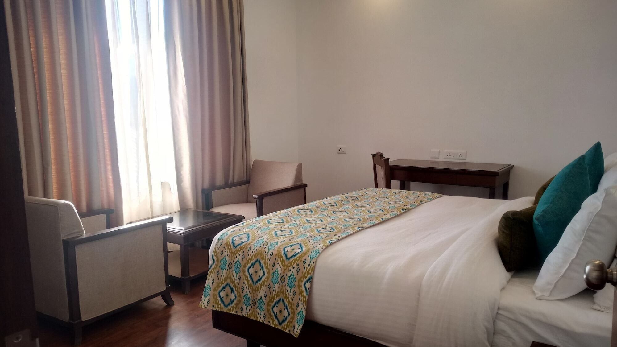 A hotel room with a bed, a chair, a small table, and a window with curtains.