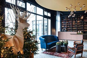 A modern interior with a large bookshelf, a blue sofa, a wooden deer sculpture, and a Christmas tree. - Leonor Hotel (Strasbourg)