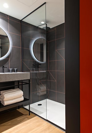 A modern bathroom with a glass shower enclosure, a vanity with a mirror, and a towel rack. - Leonor Hotel (Strasbourg)