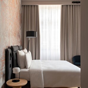 A hotel room with a bed, a round wooden side table, a floor lamp, and a chair. - Leonor Hotel (Strasbourg)