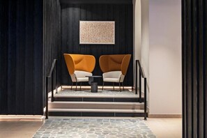 A modern lobby with a black and white color scheme, featuring a seating area with two chairs and a small table, a staircase, and a framed artwork on the wall. - Leonor Hotel (Strasbourg)