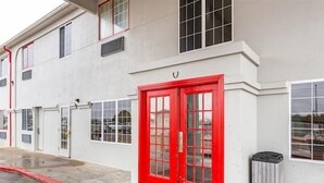 Un edificio con puerta roja, ventanas y un contenedor de basura.