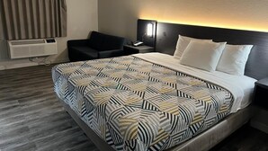 Habitación de hotel con cama, silla, mesita de noche con lámpara y equipo de aire acondicionado.