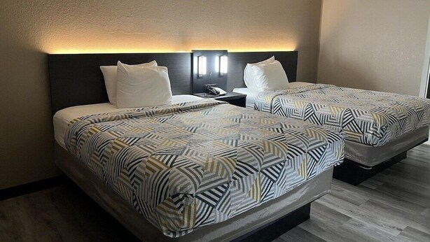 Una habitación de hotel con dos camas, una mesita de noche y una lámpara fijada a la pared.