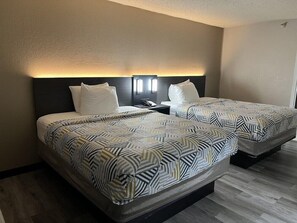 A hotel room with two beds, a nightstand, and a wall-mounted light fixture. - Motel6 Tulsa, OK - Airport (Tulsa)