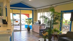 Un espace d’accueil comprenant un comptoir, des sièges, des plantes en pot et une vue sur l’extérieur à travers la porte.