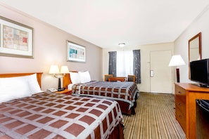 Ein Hotelzimmer mit zwei Betten, einem Schreibtisch, einem Fernseher und einem Vorhangfenster.