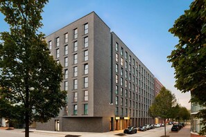 Ein modernes, mehrstöckiges Gebäude mit Backsteinfassade, großen Fenstern und einem Parkplatz mit Autos.