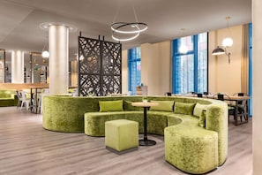 Ein modernes Interieur mit einem grünen Ecksofa, einem runden Tisch und großen Fenstern.