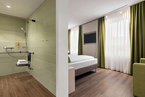 A modern hotel room with a shower, a bed, a TV, and green curtains. - Hamburg Mitte (Hamburg)