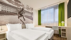 Una camera d'albergo con un letto, una scrivania, una sedia, una TV e una finestra con tende.