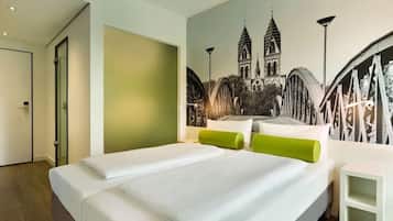 Ein Hotelzimmer mit einem großen Bett, einem grünen Kopfkissen, einem weißen Nachttisch und Wandgemälde einer Brücke und eines Turms.