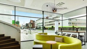 A modern interior with a curved yellow sofa, a round table, and a staircase leading to an outdoor area with a view of the city. - Premier Inn Koblenz City (Koblenz)