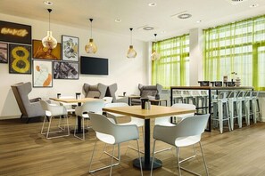 A modern cafe with tables and chairs, artwork on the walls, and a large window with green curtains. - Koblenz (Koblenz)