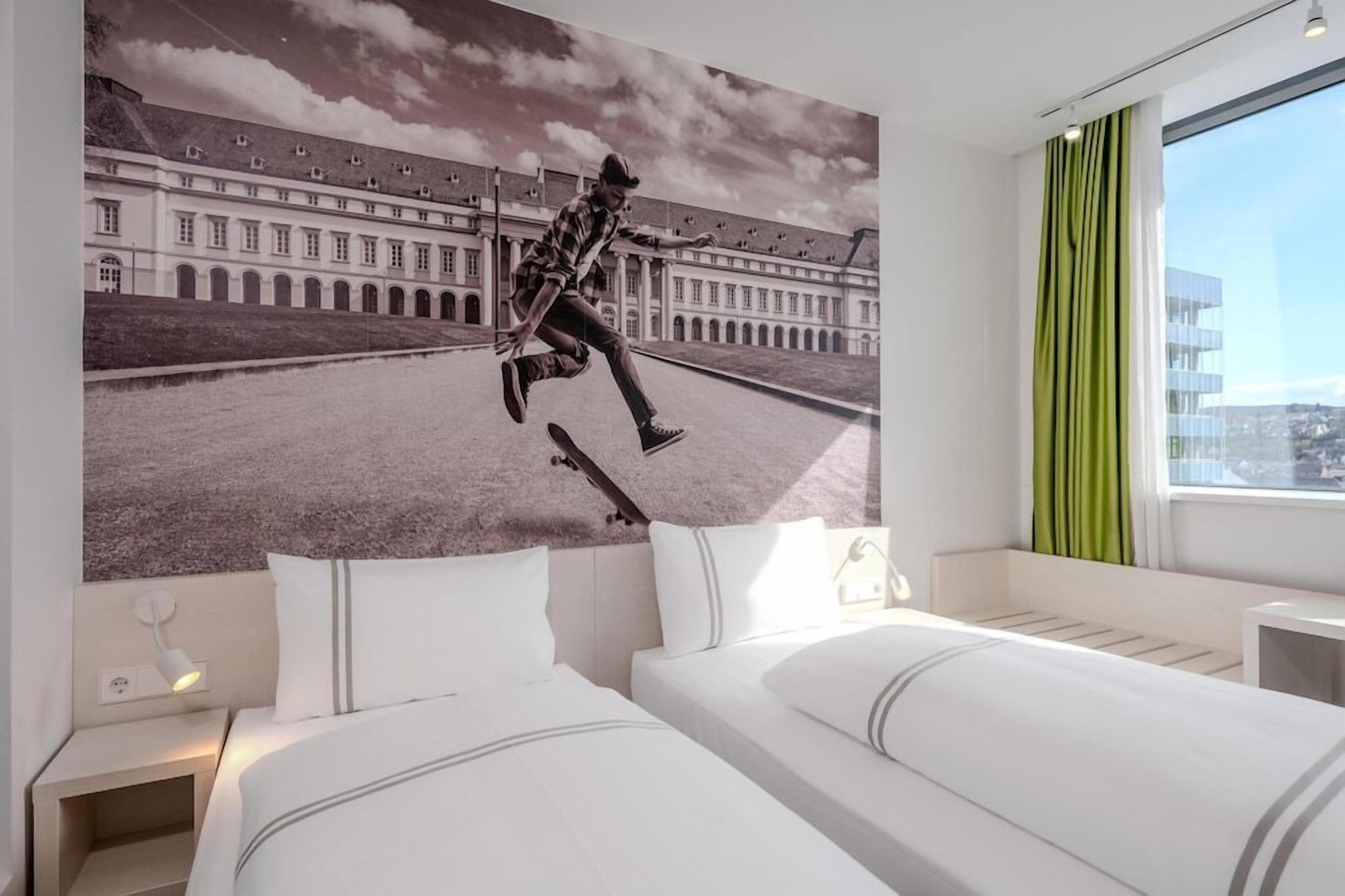 Ein Hotelzimmer mit einem Bett, einem Nachttisch, einer Wandlampe und einem großen Fenster mit Vorhängen.