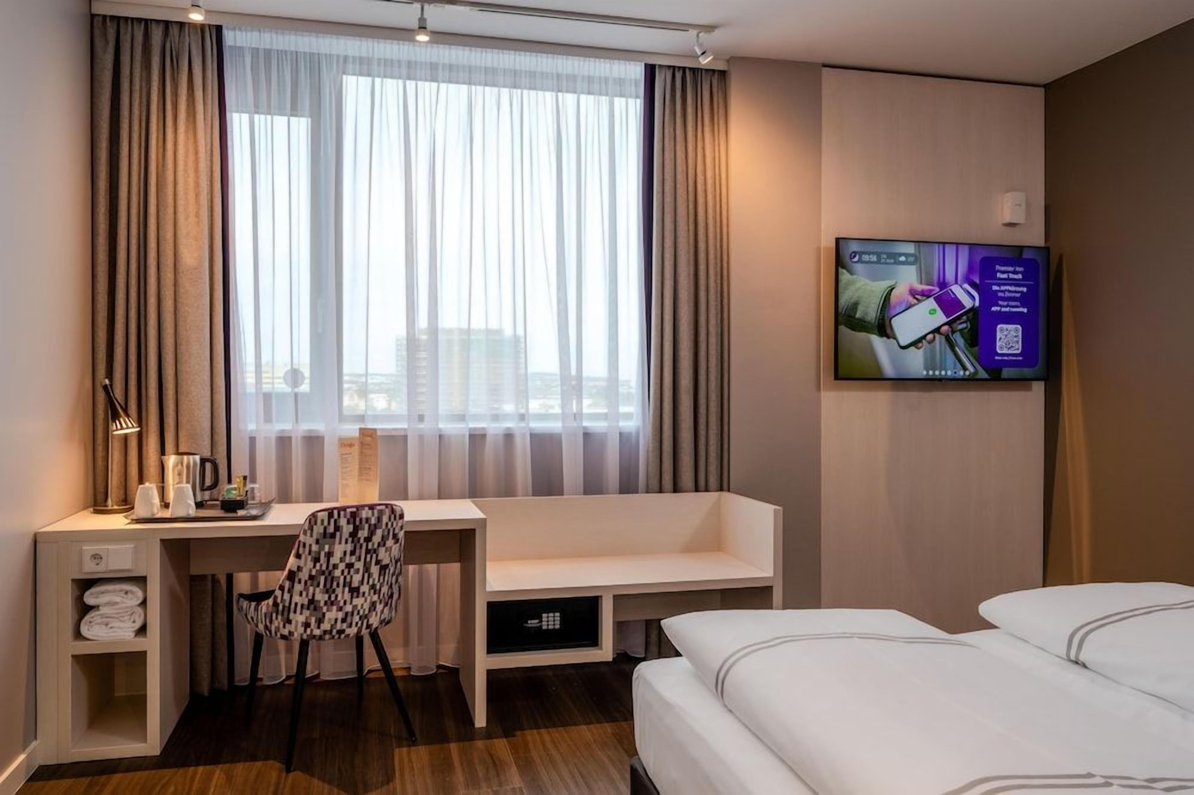 Ein Hotelzimmer mit Bett, Schreibtisch mit Stuhl, Fernseher und einem Fenster mit Vorhängen.