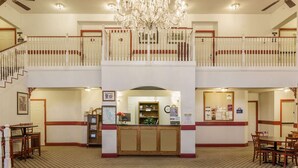Un hall d’hôtel comprenant un comptoir d’accueil, deux niveaux d’espaces aménagés avec des sièges, un lustre et un escalier.