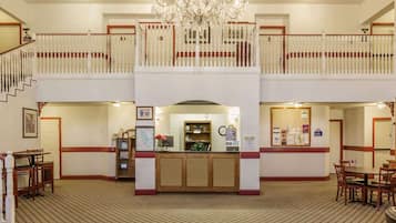 A hotel lobby with a reception desk, two floors of seating, a chandelier, and a staircase.