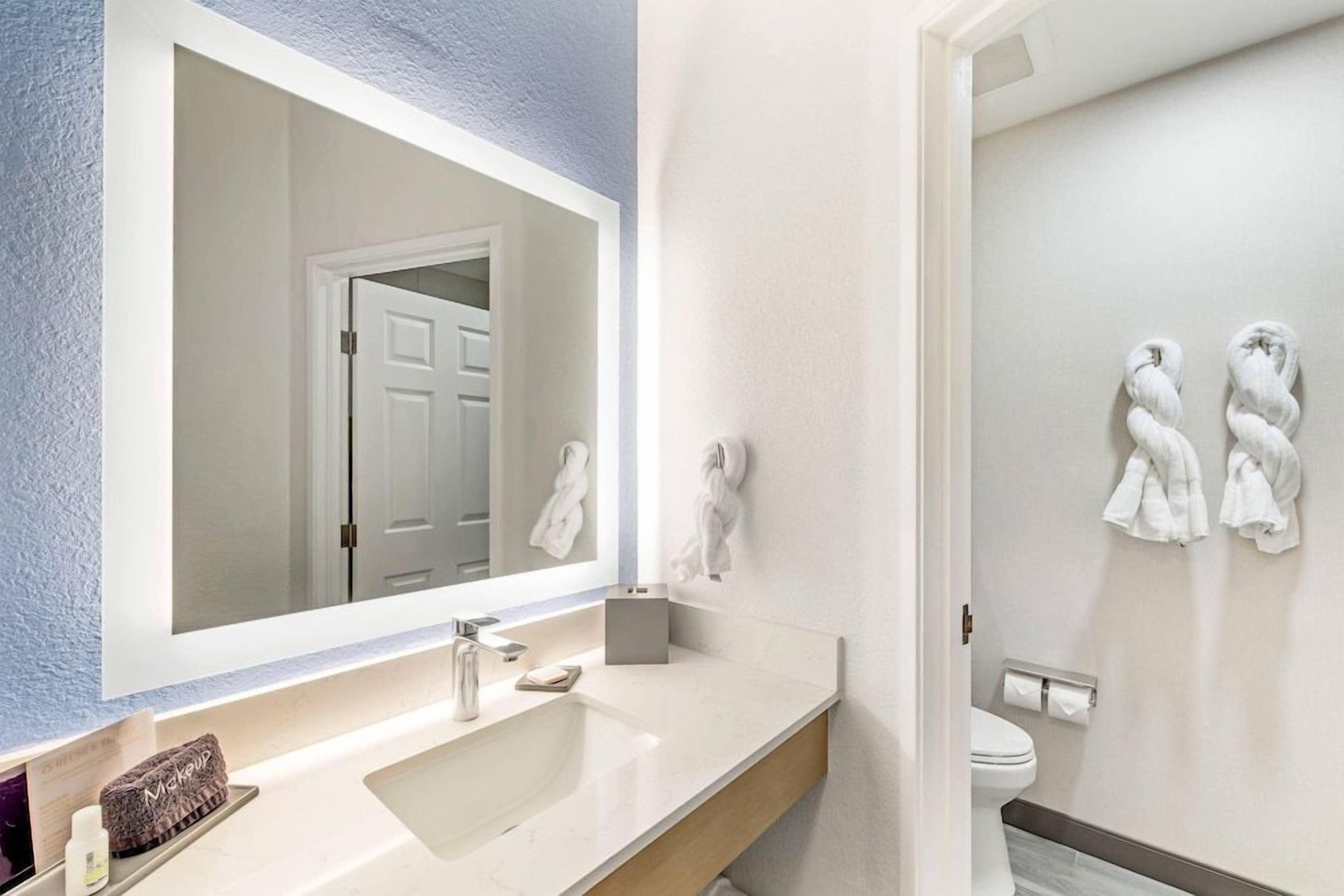 A bathroom with a large mirror, a sink, a toilet, and towels on the wall.