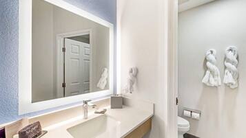 A bathroom with a large mirror, a sink, a toilet, and towels on the wall.