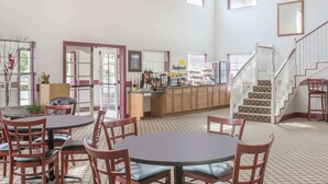 Un grand espace de salle à manger avec plusieurs tables et chaises, un comptoir de cuisine où sont disposés des articles pour le petit-déjeuner, et un escalier menant à un niveau supérieur.