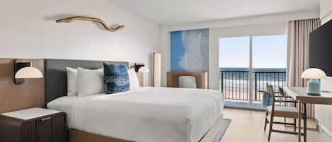 Habitación de hotel con una cama grande, mesitas de noche, un escritorio con silla y vista al océano.