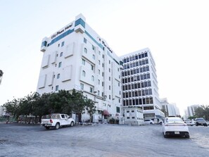 Un hotel de varios pisos con un cartel llamativo que dice 'City Plaza Hotel', un estacionamiento con varios vehículos y un cielo despejado.