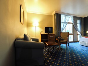 Habitación de hotel con sofá, una mesita, televisor, minibar, sillón y cama.