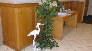 Un mostrador de recepción con detalles de madera, una planta en maceta con follaje verde y una estatua decorativa de un pájaro blanco.