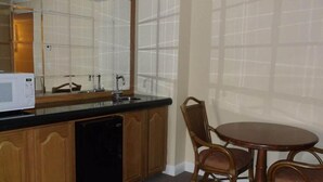 Cocina con microondas, pileta y armarios de madera. Hay una mesa de comedor con sillas y una ventana con persianas.