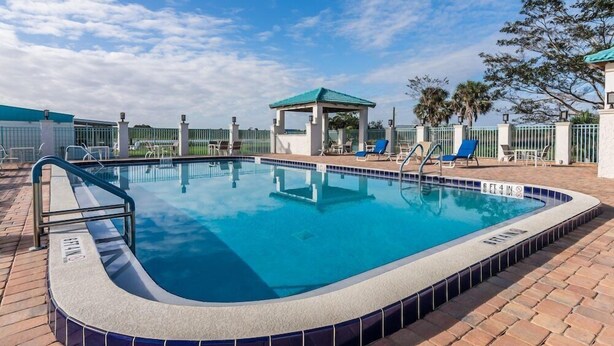 Una piscina con borde de azulejos, una zona de estar cubierta y un perímetro cercado.