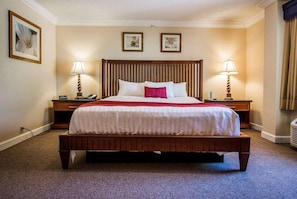 Une chambre d’hôtel avec un grand lit, deux tables de chevet, une tête de lit en bois et deux lampes fixées au mur.