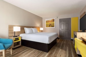 Une chambre d’hôtel comprenant un lit, des tables de chevet, un bureau, une chaise, une télévision et une porte.
