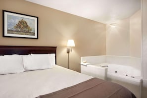 Une chambre d’hôtel avec un lit, un tableau au mur, une table de chevet avec une lampe et une baignoire.