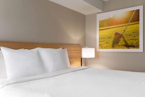 Une chambre d’hôtel avec un lit, une tête de lit, une lampe fixée au mur et un tableau représentant un terrain de golf.