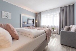A modern bedroom with a bed, a grey sofa, a bedside table, a lamp, and a window with curtains. - Yggotel Solsort (Essen)