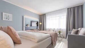 A modern hotel room with a large bed, a sofa, a small table with a plant, and a TV on the wall.