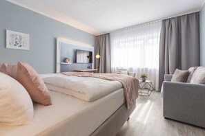 Ein modernes Hotelzimmer mit einem großen Bett, einer Couch, einem kleinen Tisch mit einer Pflanze und einem Fernseher an der Wand.