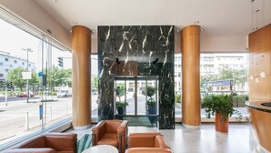 A lobby with a marble wall, leather seating, and a view of the street.