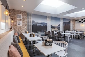 A modern restaurant with a brick wall, white tables, and a mural of a mountainous landscape. - Yggotel Solsort (Essen)