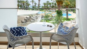 A balcony with two white wicker chairs, a small round table with a glass and sunglasses, and a view of a pool and palm trees. - TUI Blue Palm Beach Hammamet (Hammamet)