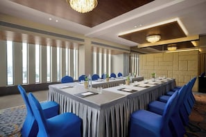 Un salón de conferencias con una larga mesa, sillas azules y un candelabro.